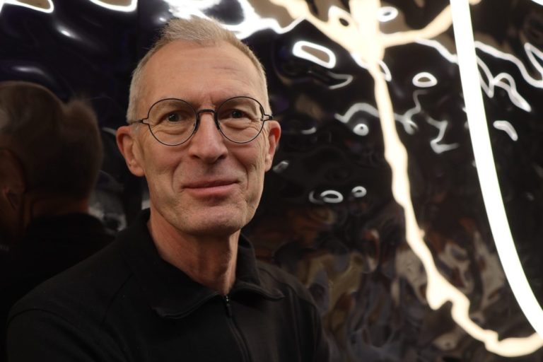Porträt von Stefan Lieschke Mann in Anzug mit Brille, freundliches Lächeln, dunkler Hintergrund.